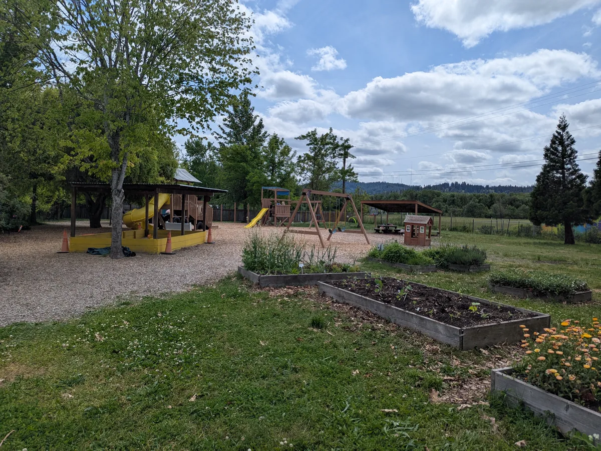 Wide view of playground with swings, sandbox, and garden beds