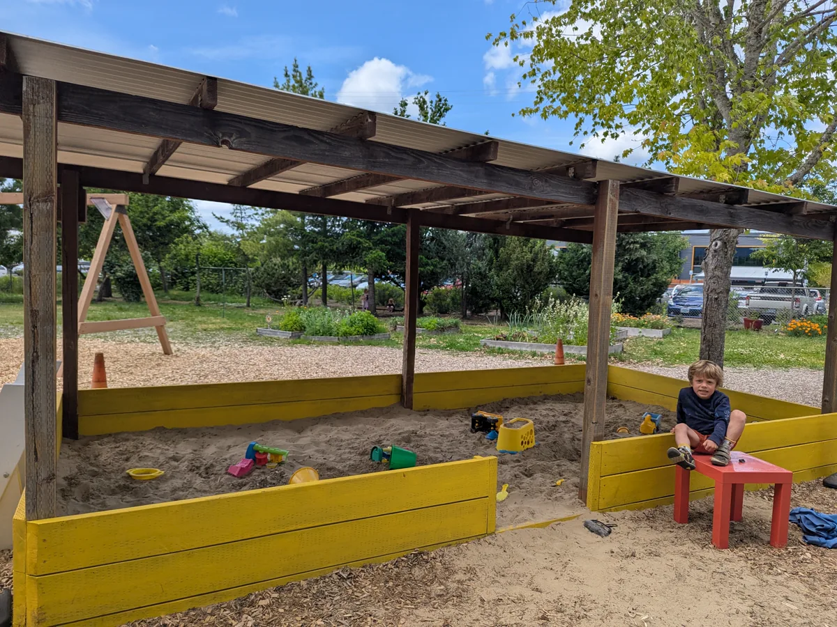 Newly painted yellow sandbox with covered pergola structure